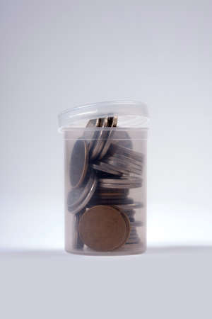 Coins in an open small transparent plastic piggybank like container, concept of saving money, tiny...