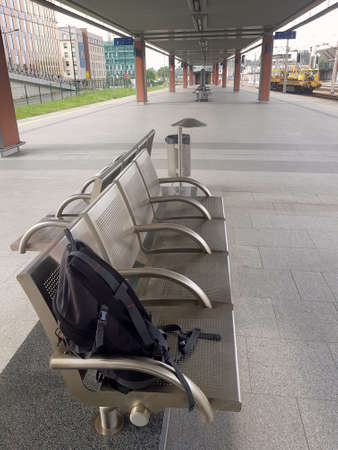 A single lonely backpack left behind, abandoned on a bench on a train station. Forgotten luggage or tourist leaving a bag behind in a public area with nobody in sight or travelling solo conceptの写真素材
