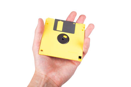 Single bright yellow floppy disk, pastel computer diskette being held in hand, shown, presented to the viewer. Old tech vintage historical data storage save icon concept. Isolated on white, copy spaceの写真素材