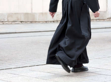 Catholic priest in the black cassock walking on the street solo, only legs visible. Clergy, faith, christianity and calling abstract concept