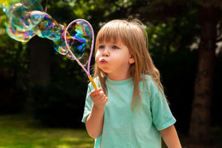 Little child, girl blowing huge bubbles alone, portrait outdoors. Young kid with puffed cheeks blows big bubbles outside, closeup shot Playing, fun activities for children, happiness concept lifestyleの写真素材