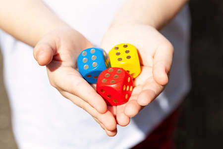Little child holding three colorful wooden dice showing six in her small hands, closeup. Multi colored game dice with number 6 on them. Fortune, success, winning throw luck abstract concept, good oddsの写真素材