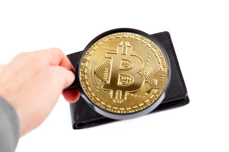 Closer look at a crypto currency wallet, hand holding a loupe revealing a golden bitcoin coin...