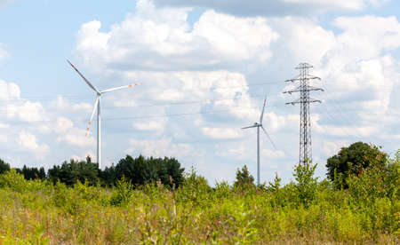 Two wind turbines and power lines in a green field, country landscape shot, sunny weather. Green...