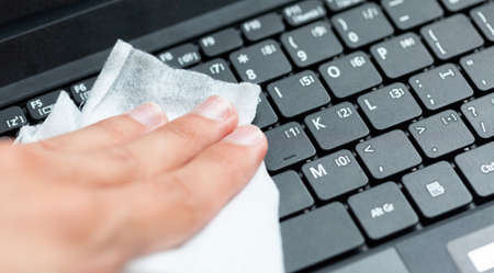 Hand disinfecting, sanitizing a modern laptop keyboard using a wet wipe. Cleaning notebook keys with a damp tissue, closeup. Office workspace hygiene practice, covid 19, corona virus safety practicesの写真素材