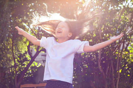 Happy young girl alone, little cheerful school age child jumping up, flying dispelled hair, arms spread, sunlight, outdoors portrait. Childhood and happiness, freedom, fun activity outside, lifestyleの写真素材