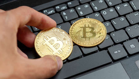 Hand placing two bitcoin gold coin symbols on a modern laptop keyboard. Bit coin cryptocurrency logo, crypto trading market, simple online digital currency exchange abstract conceptの写真素材