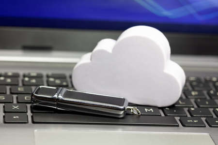 Cloud data storage technology, storing data in the cloud abstract. Cloud and a usb memory stick, pen drive laying on a laptop keyboard. Online private personal data backup service tech simple conceptの写真素材