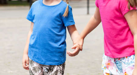 Two anonymous school age children, sisters, siblings together, one girl grabbing, taking other girls hand, kids holding hands on the street. Family, togetherness and care, lifestyle simple conceptの写真素材