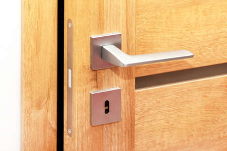 Door to a darkened room open a little, metal handle with a key hole closeup, inside shot, modern interior house wooden door gap detail. Peek concept, nobody. Household protection, safety and securityの写真素材