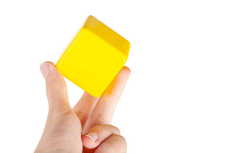 Hand holding up a simple plain yellow floating hovering cube element or node grabbing it between fingers, isolated. Network app, application interface smart human interaction gesture abstract conceptの写真素材