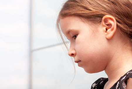 Sad little school age girl deep in thought, pensive expression face closeup, melancholic portrait, copy space, side view. People expressions abstract, mental health, development psychology conceptの写真素材