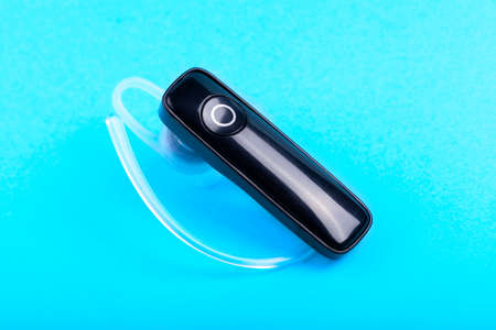 Single ergonomic wireless earpiece, hands free mono earbud, safe hands-free phone call accessories, one earphone object on blue background, Phone smartphone wireless gadgets concept, nobodyの写真素材