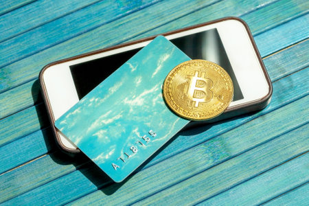 Bitcoin gold coin and a gift card, credit card laying on top of a modern smartphone screen. BTC...
