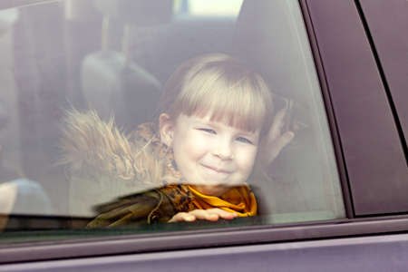 Little girl, child sitting inside the car seen from the outside. Young kid peeking from the vehicle window, portrait, closeup. Means of transport, children traveling, transportation, motion sicknessの写真素材