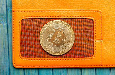 One single bitcoin gold coin symbol laying on a stylish trendy orange wallet top view, macro,...