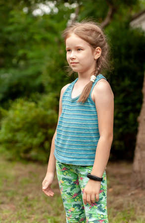 One young proud confident school age girl smiling, happy child wearing a fitness band outside, fit smart watch, standing straight, vertical outdoors portrait children and technology concept, lifestyleの写真素材
