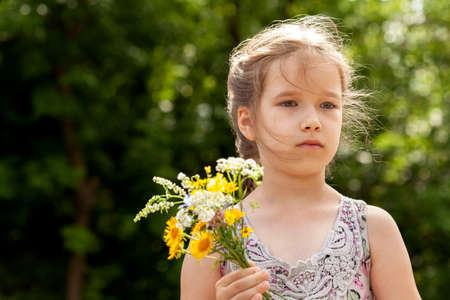 School age child, little young elementary age girl holding a small bouquet of herbs and field flowers, summer portrait, face closeup, one person. Copy space, blurred background, children and natureの写真素材