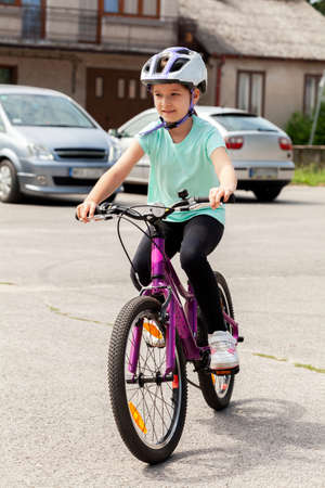 Young happy little child, school age girl riding a bike in a bicycle helmet. Outdoor healthy activities, cycling sports and recreation concept, vertical shot, one person. Child learning to ride a bikeの写真素材