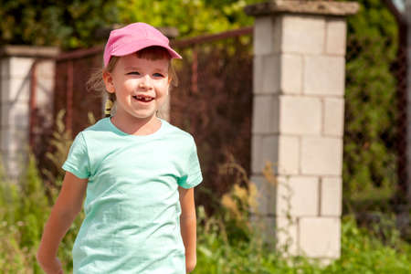Happy young school age child, little cheerful girl smiling, laughing simple portrait outdoors, face closeup, copy space, blurred background. Kid missing a tooth laughing, mouth open, daytime, summerの写真素材