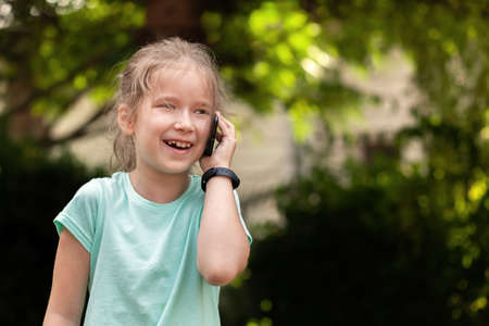 Young school age child talking on her mobile phone, little girl speaking, holding a smartphone next to ear, smart band on hand portrait closeup, copy space. Telecommunications, children and technologyの写真素材