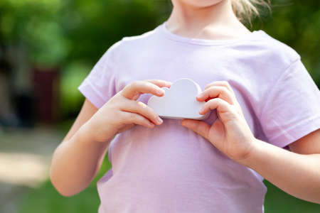 Young anonymous child, elementary school age girl holding a simple white cloud model in hands,...