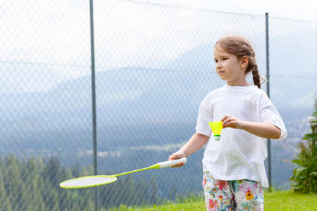 Young sporty active elementary school age girl playing badminton, holding a racket and a shuttlecock ready to serve. Outdoors portrait, closeup, background copy space, one person. Sport and recreationの写真素材