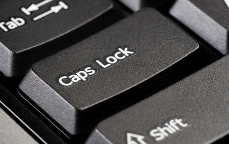 Single caps lock key on a simple black desktop PC computer keyboard, object detail, extreme closeup. Using capital letters, typing in all caps, screaming, shouting, emphasis abstract concept, nobodyの写真素材