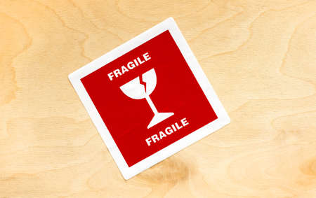 Red fragile cargo package sticker label on a wooden box crate container, detail, closeup, top view,...
