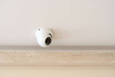 One single round security camera on a ceiling in a bright room, CCTV cam object detail, closeup,...