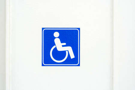 Simple square wheelchair symbol sticker, label on a white wall, people with disabilities accessibility issue concept, blue wheelchair access sign closeup front view, nobody, no peopleの写真素材