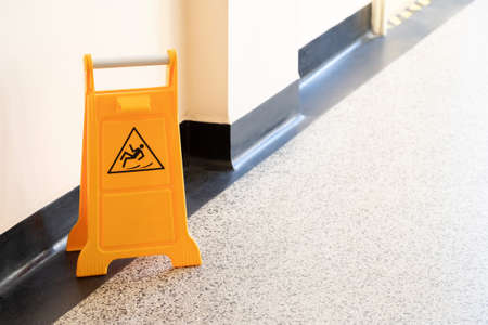 Caution wet floor orange fold out sign without text in a bright corridor, closeup detail Slipping man symbol, object up close, nobody, copy space Accidents, at work, cleaning services abstract conceptの写真素材