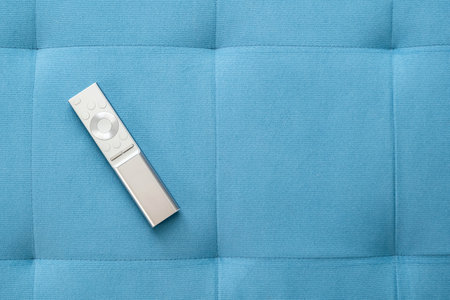 One single simple sliver smart TV remote control laying on a blue sofa pillow at home, object top view, closeup, nobody. Leisure, rest, watching TV symbol, concept, copy space background, no peopleの写真素材