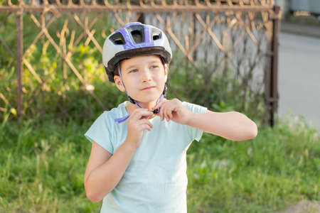 School age biker girl putting on or taking off, fastening her protective biking helmet, portrait, face closeup, copy space. Children, kids biking, cycling safety and protection from injuries. Sportsの写真素材