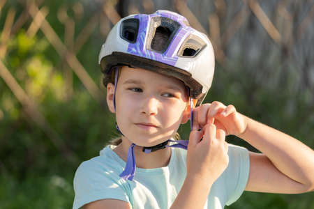 School age biker, child taking off or putting on a protective biking helmet, young cyclist portrait, face closeup, girl fastening her helmet. Blurred background, children and biking, cycling, sportsの写真素材