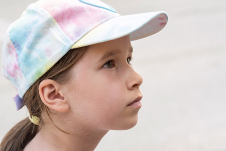 Young elementary school age girl, European, Caucasian child portrait, face closeup, side view, detail, real people lifestyle, one person, copy space. Kid in a baseball cap, up close shot, one personの写真素材
