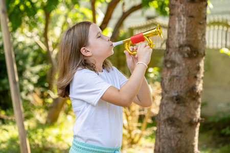 Elementary school age girl playing a toy trumpet prop, holding it in hands doing a bugle call signal. Simple calling, call to arms, signalling abstract concept. Children and music education, soundsの写真素材