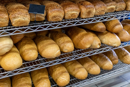 Various types of golden-brown freshly baked bread neatly arranged on metal racks, fresh bakery bread...