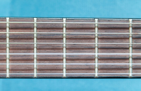 Close-up view of a guitar fretboard, metal frets, strings against a blue background, object macro...