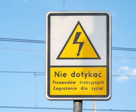 Caution sign with a warning message in Polish against touching overhead electrical wiring indicating...