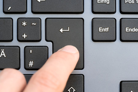 Finger captured in the moment of pressing the Enter key on a sleek modern design keyboard,...