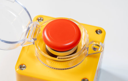 Close-up shot of a red emergency stop button with a protective clear casing mounted on a yellow...