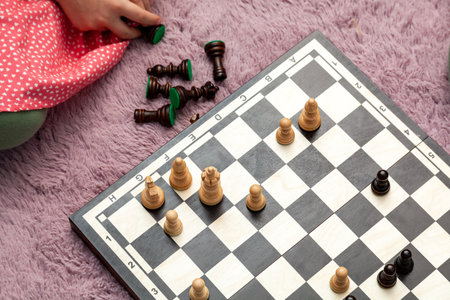 Young child playing chess pieces laid out on the ground, soft purple carpet the chessboard reveals...