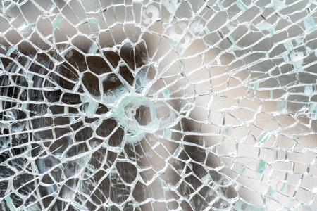 Closeup detail macro view of cracks spreading across a shattered glass panel, single point damage,...