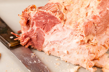 Sliced ham rests on a cutting board next to a carving knife, partially carved with succulent meat...
