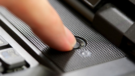 Finger pressing a generic round dark black power button on a simple office laptop, closeup detail,...