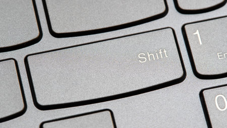 Man pressing the shift key on a modern laptop computer keyboard closeup top view, one person. Shift...