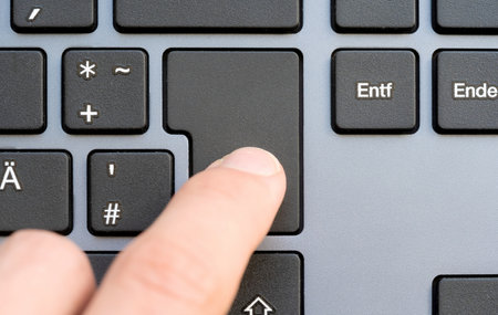 Finger pressing a simple blank enter key on a computer keyboard, empty button with copy space for text or a symbol, close-up. Modern workspace, top view, from aboveの写真素材