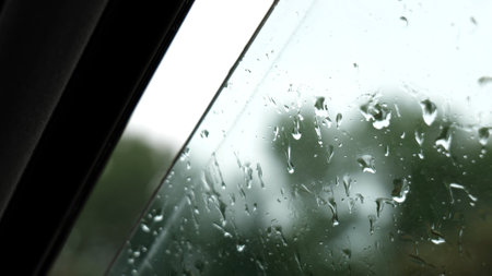 Rain falling on wet open car window, close-up of raindrops on vehicle glass, car interior during rain, detailed shot of rainwater on window, stormy weather driving, rainy day vehicle interior closeupの写真素材