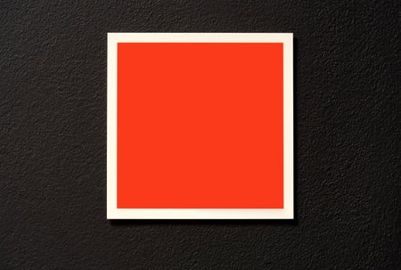 Blank red square label sticker on a black wall indoors, empty framed warning sign template, white border minimal frame sign template, symbol copy space, front view isolated design element for brandingの写真素材